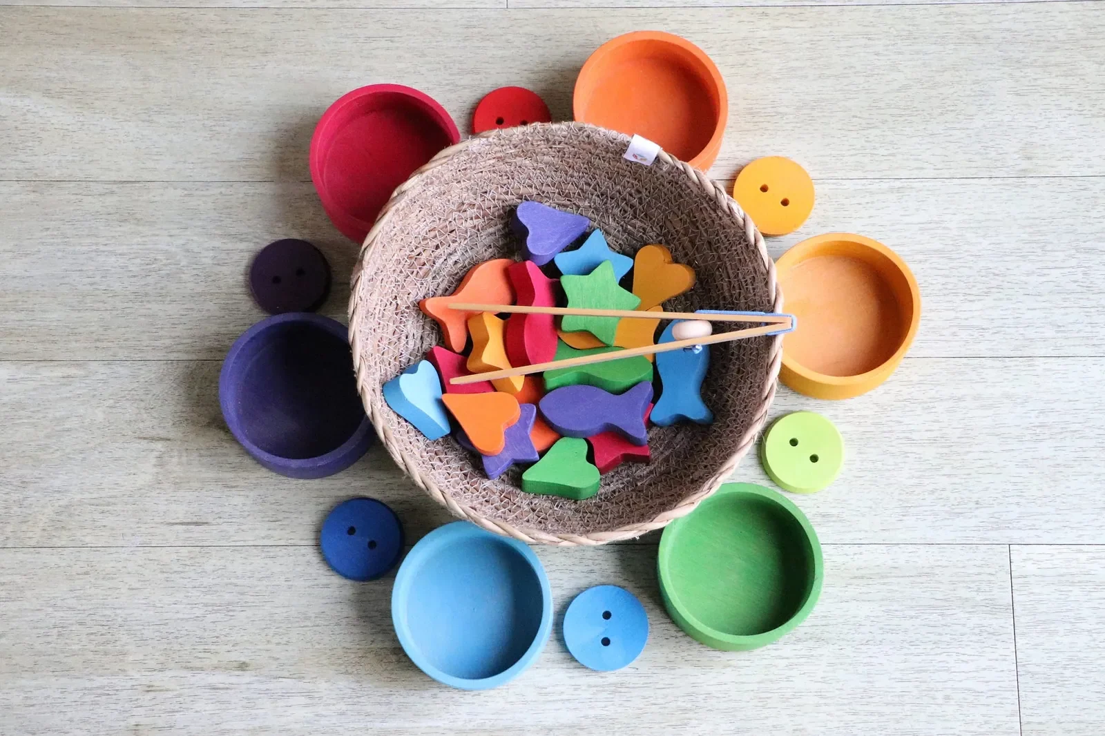 Wooden bowl of coloured toy shapes and buttons on a table, seen from above
